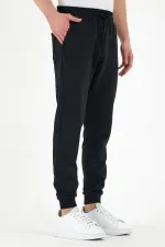Pantalon de survêtement noir pour homme, coupe classique, avec étiquette, poches arrière et latérales.
