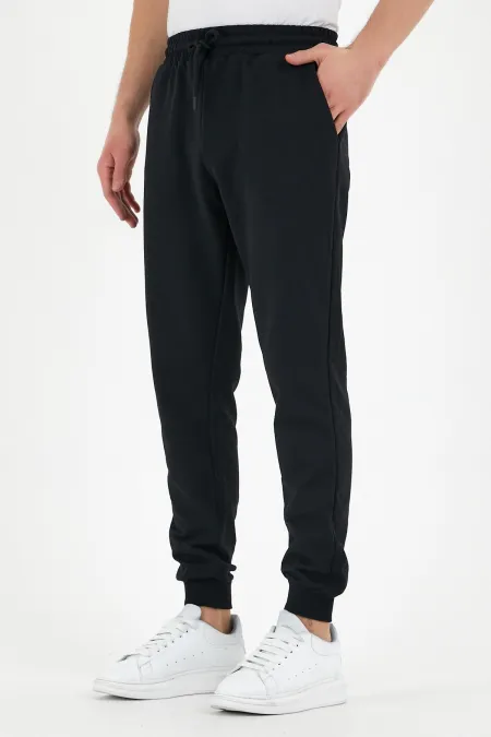 Pantalon de survêtement noir pour homme, coupe classique, avec étiquette, poches arrière et latérales.