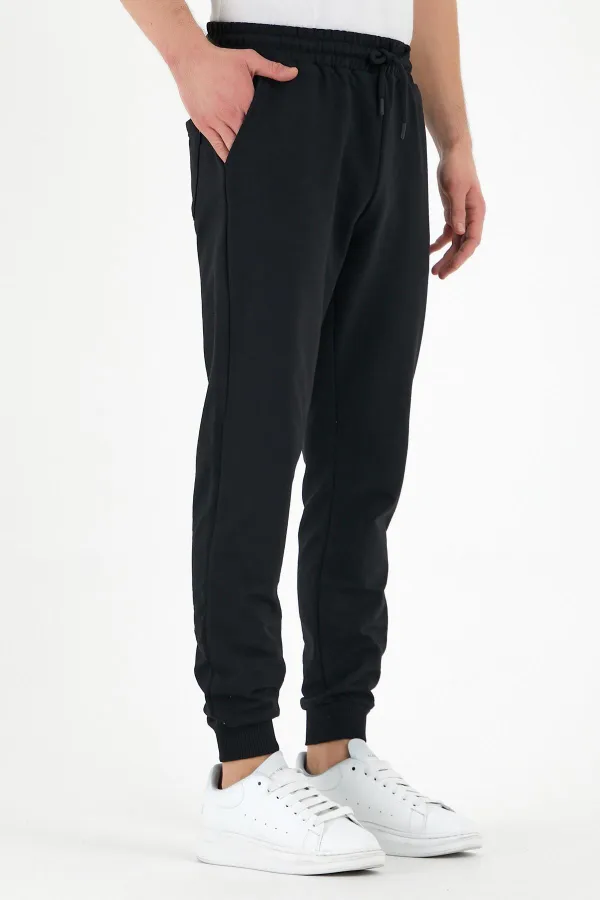 Pantalon de survêtement noir pour homme, coupe classique, avec étiquette, poches arrière et latérales.