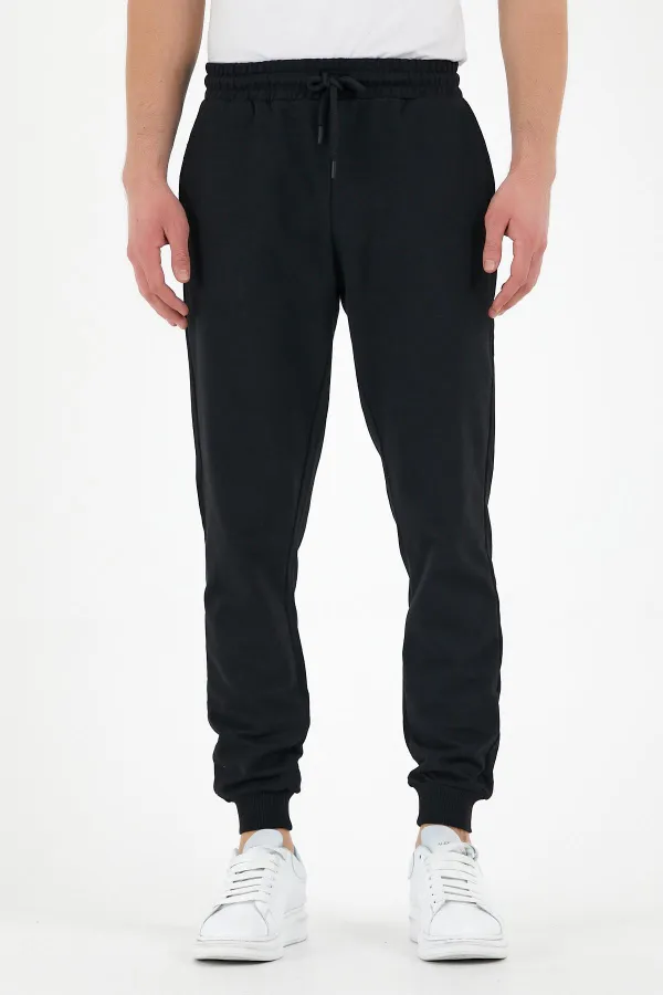 Pantalon de survêtement noir pour homme, coupe classique, avec étiquette, poches arrière et latérales.