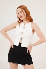 Chemisier blanc en gros avec détail de broche en nœud laqué et manches zéro